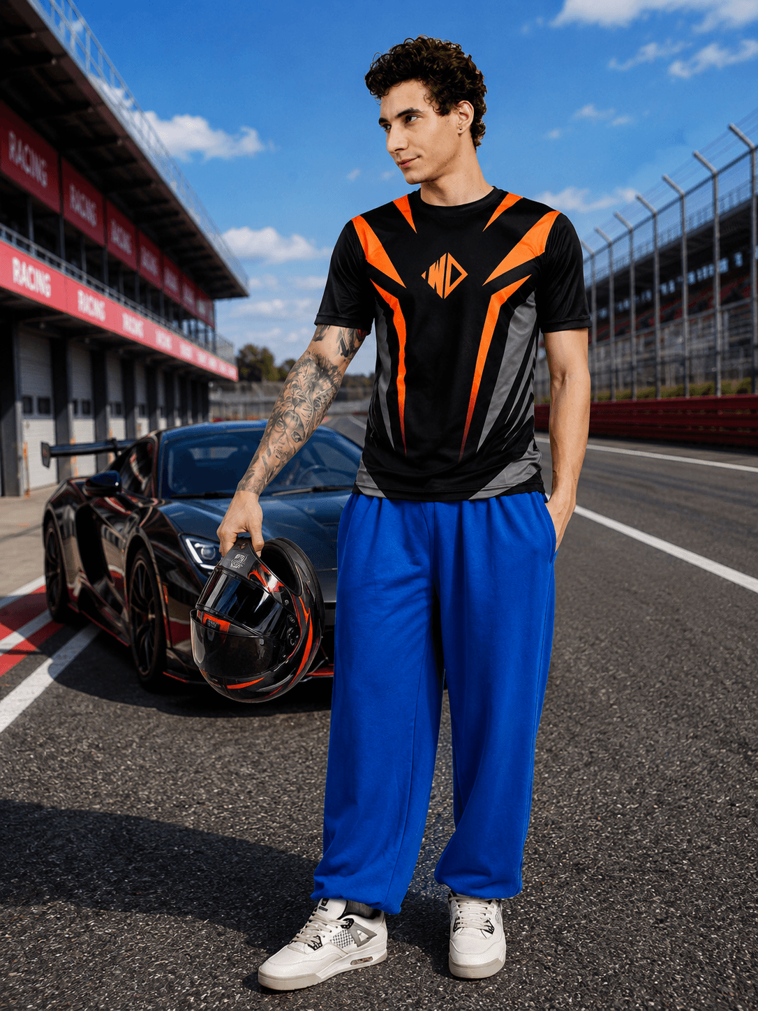 Model wearing NITRO SHIFT ATHLETIC T-SHIRT BLACK with blue pants by a racing car on track.