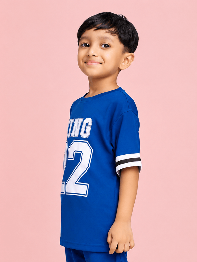KING 22 VARSITY T-SHIRT FOR BOYS GIRLS BLUE worn by a smiling boy in a vibrant blue shirt with sporty graphics.