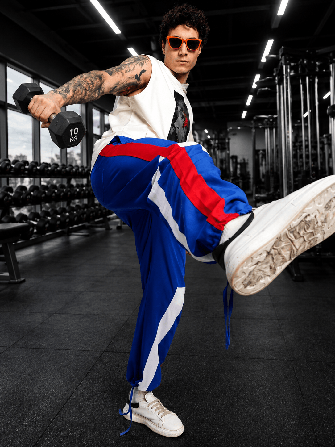 Man wearing RETRO RUNNER RELAXED-FIT JOGGERS BLUE MULTI doing a workout in a gym, holding a dumbbell and striking a pose.