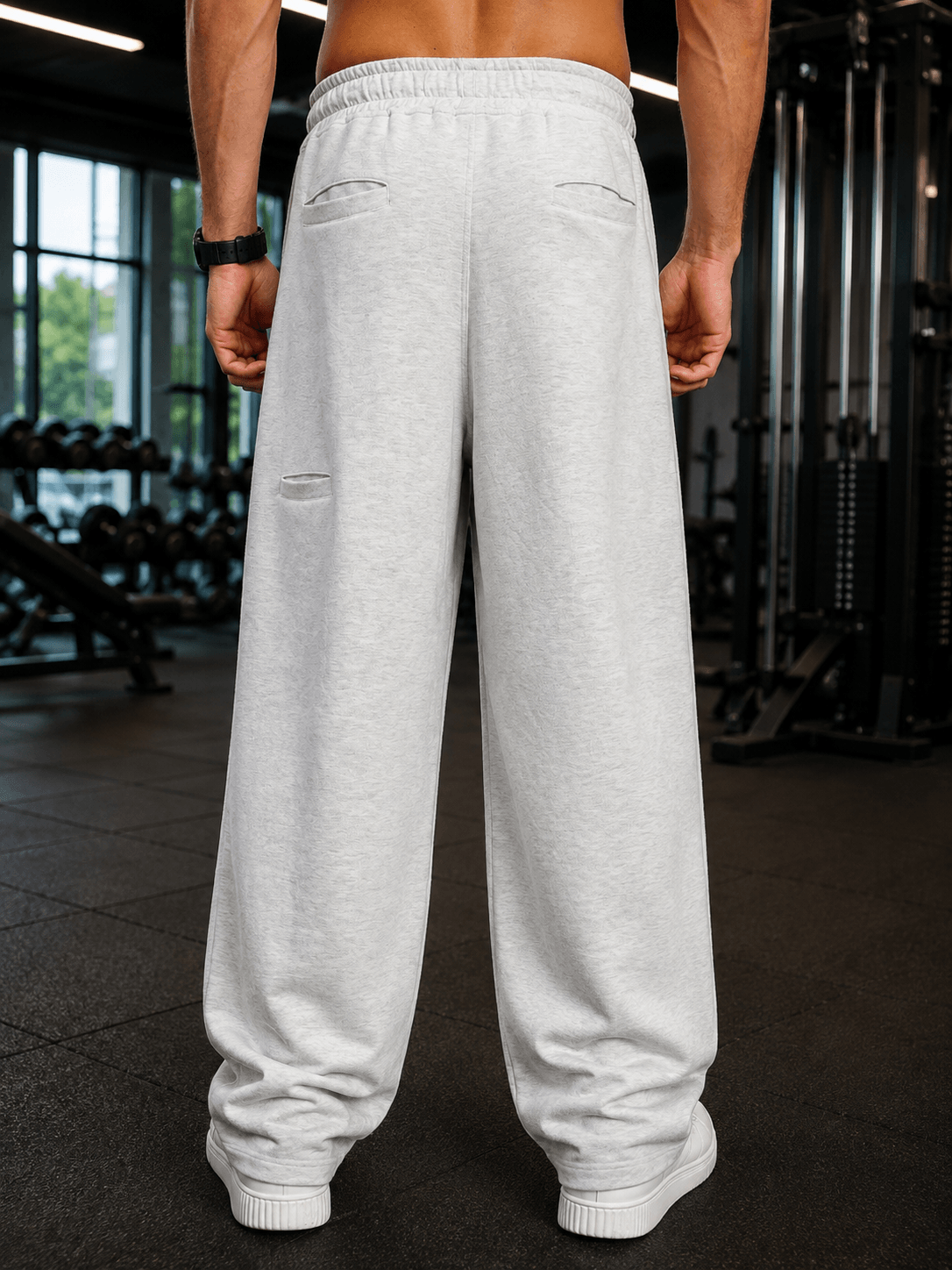 Back view of a man wearing CARABINER UTILITY BAGGY JOGGERS MELANGE GREY in a gym setting.