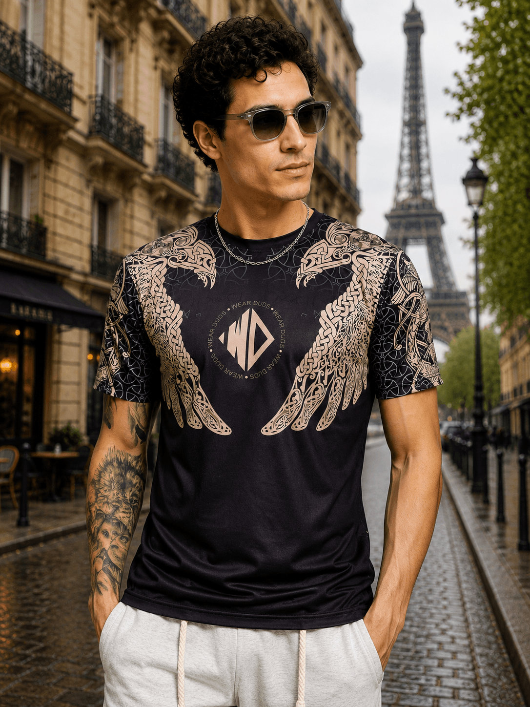 AURA OF ASGARD REGULAR T-SHIRT BLACK worn by a man in front of the Eiffel Tower, featuring unique wing design.