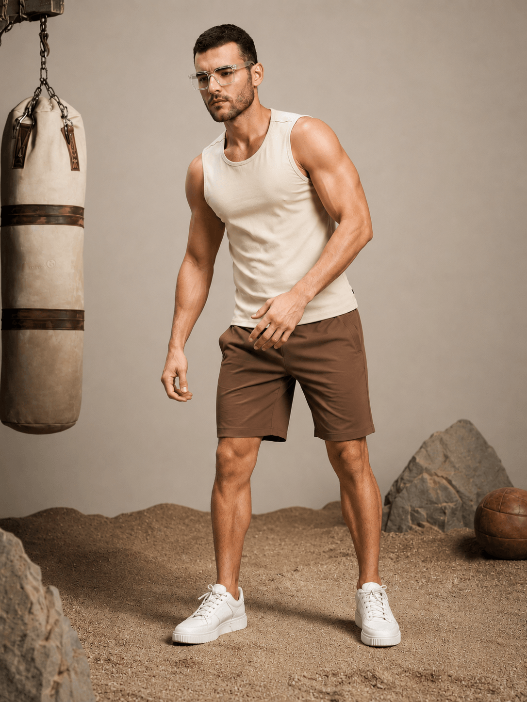Man wearing SLIM-FIT SOLID REGULAR SHORTS BROWN, stylish and modern, paired with a sleeveless top and white sneakers.