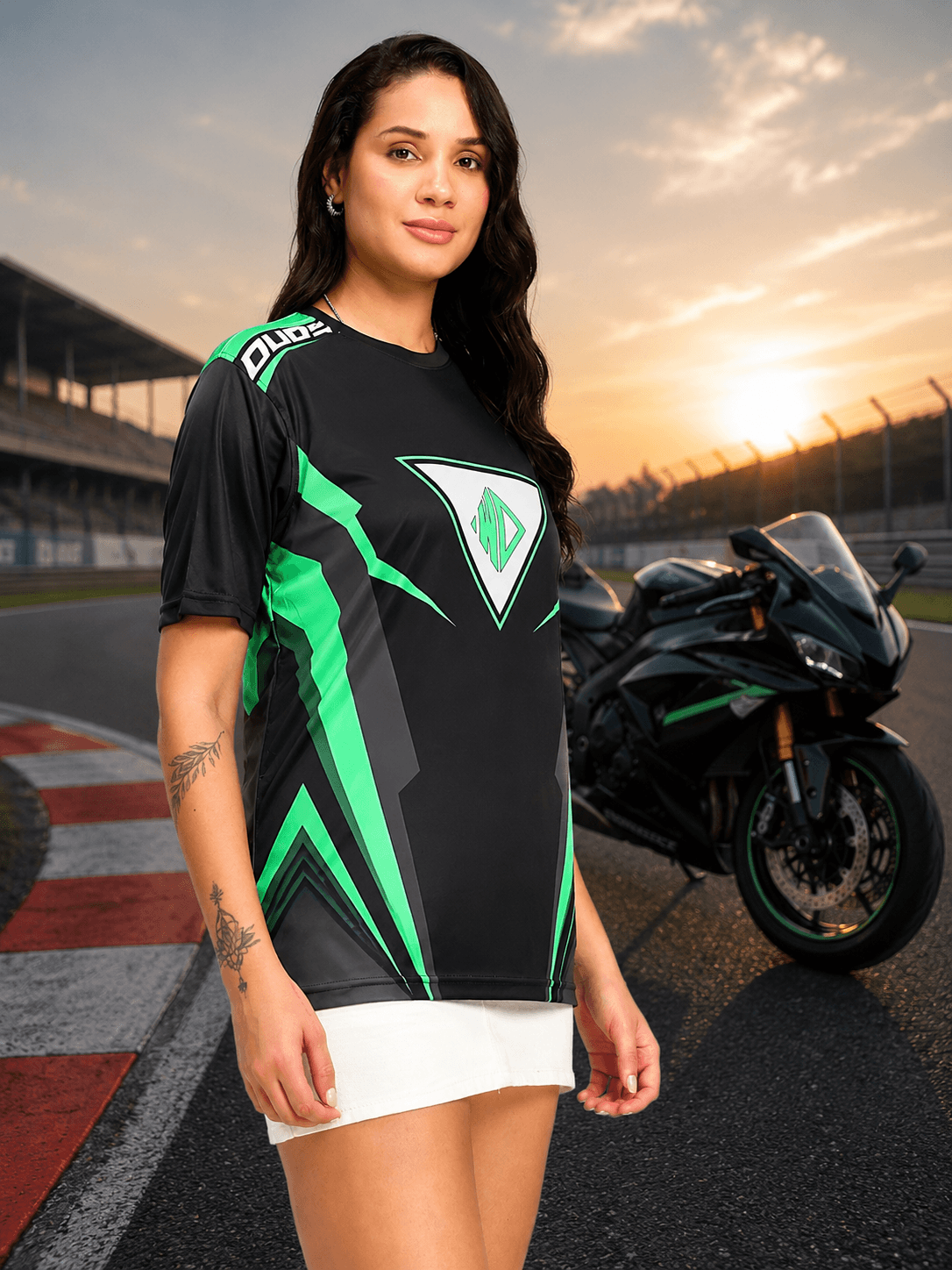 Women Apex Racing Regular T-Shirt Black worn by model in front of motorcycle on racetrack at sunset.