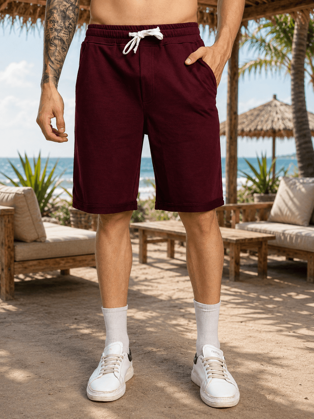 DRIVE MONOCHROME RELAXED FIT SHORTS MAROON worn by a model in a tropical setting with beach and palm trees.