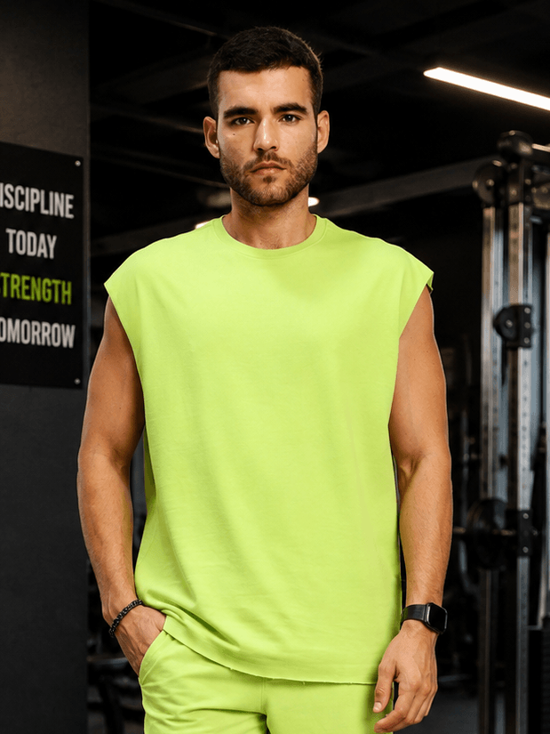 DRIVE MONOCHROME SLEEVELESS T-SHIRT NEON GREEN worn by a model in a gym setting, showcasing vibrant color and modern style.