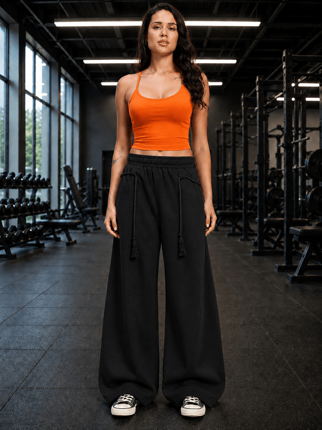 A woman wearing a WOMEN SEAMLESS COTTON CROP-TOP ORANGE with black wide-leg pants in a gym setting.