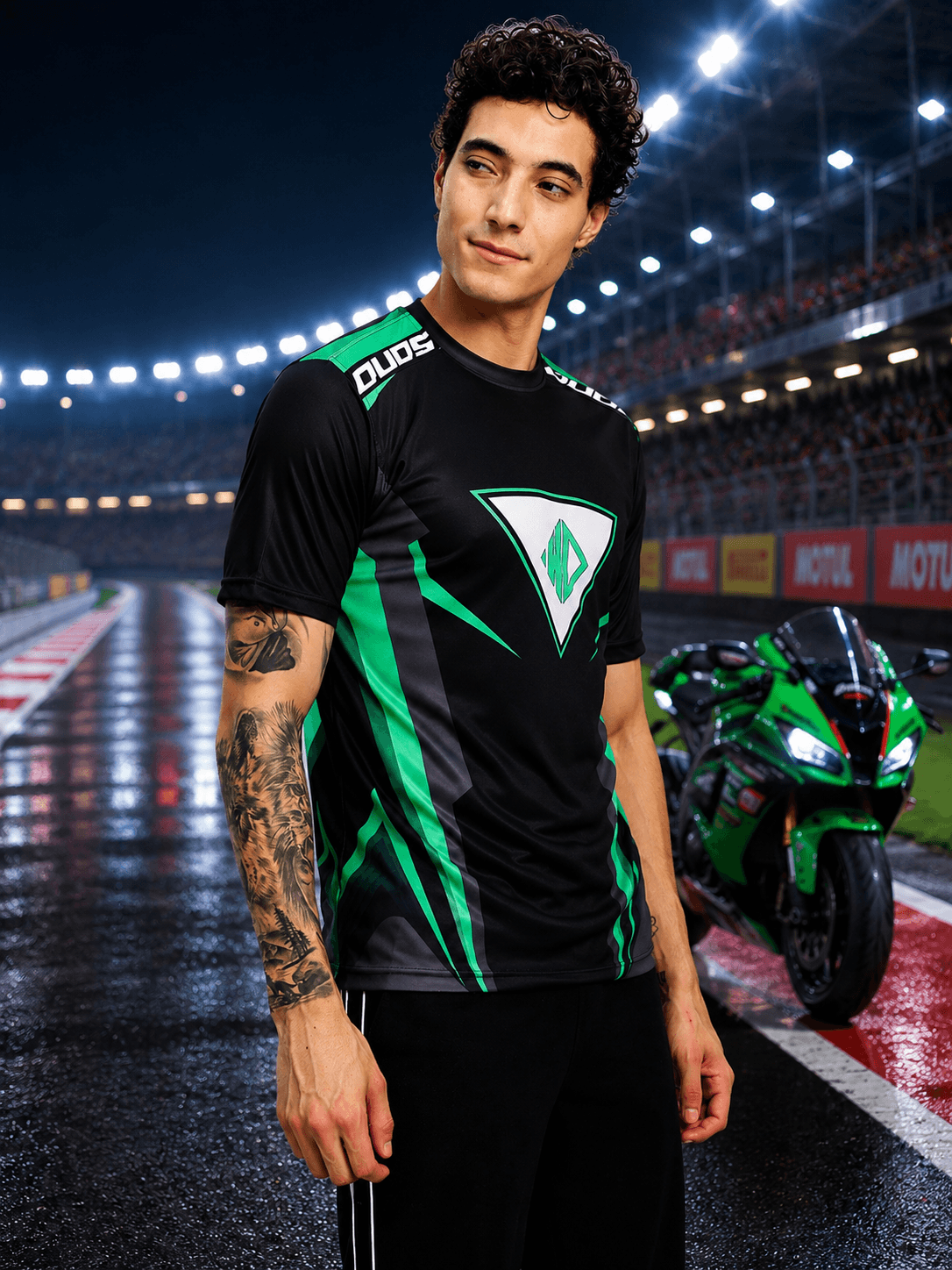 Model wearing APEX RACING T-SHIRT BLACK with green design at a racetrack.