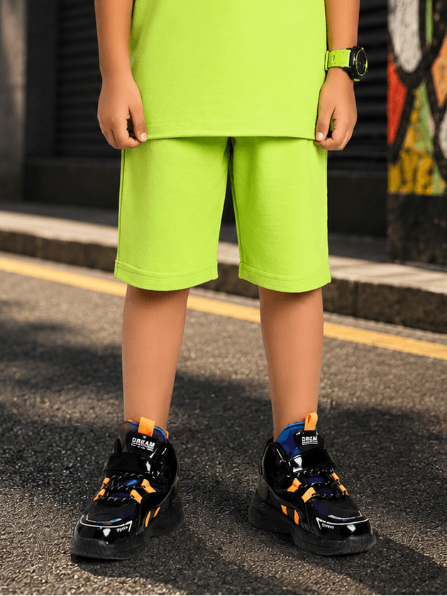 NEON RUSH SHORTS FOR BOYS GIRLS NEON GREEN worn by a child with black sneakers on a street.