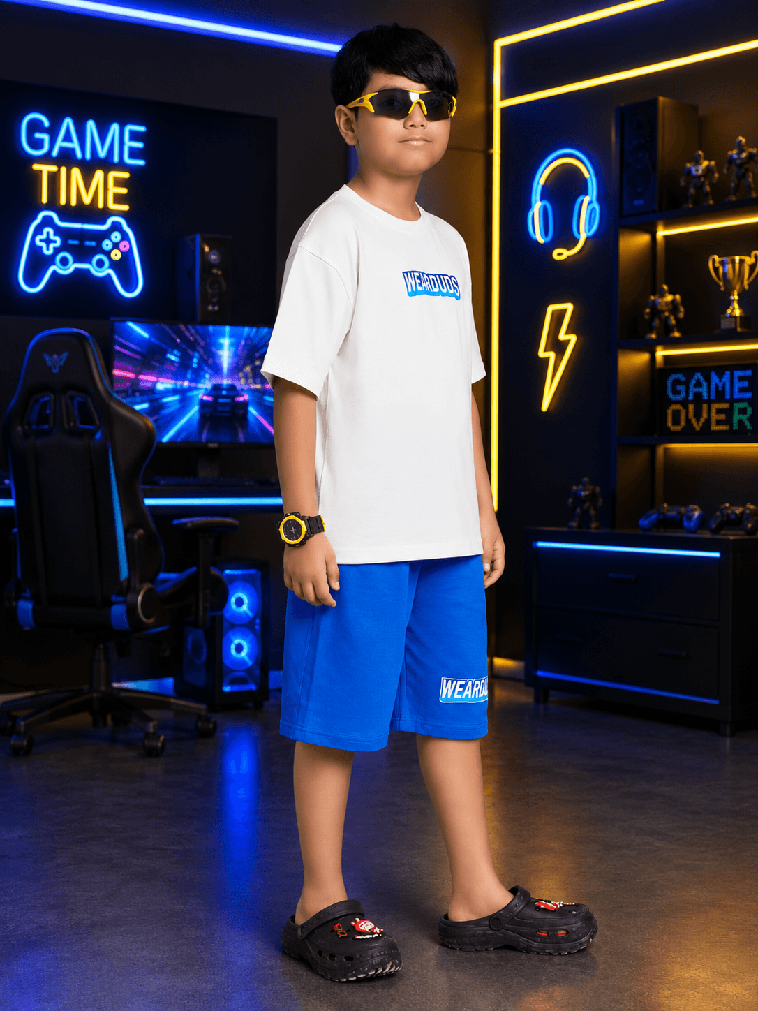Boy wearing FUSION SHORTS FOR BOYS GIRLS BLUE in a modern gaming room with neon lights.