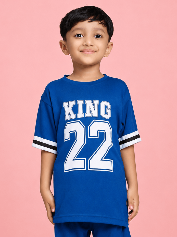 KING 22 VARSITY T-SHIRT FOR BOYS GIRLS BLUE worn by a smiling boy against a pink background.