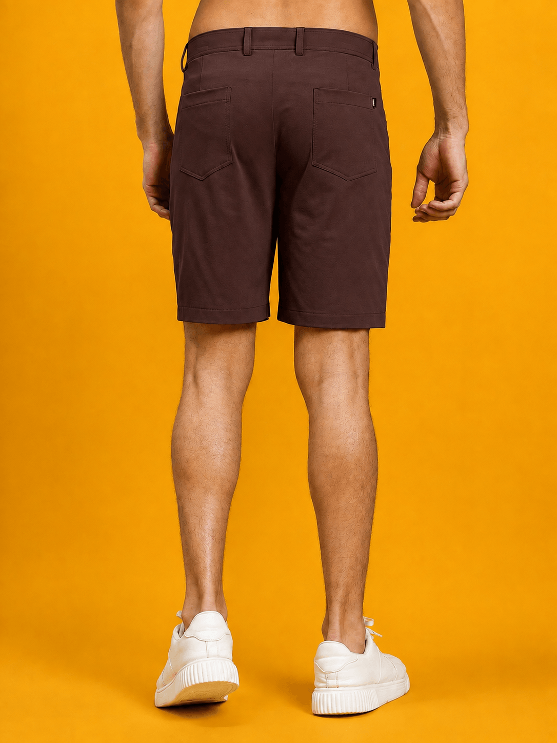 A man wearing PRIME FIT PERFORMANCE REGULAR SHORTS MAROON, showcasing the back view against a yellow background.