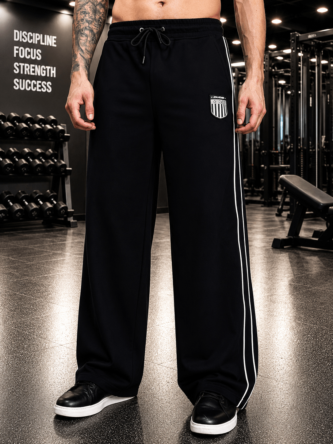 A model wearing BLACK OUT-FIT JOGGERS BLACK in a gym setting with weights in the background.