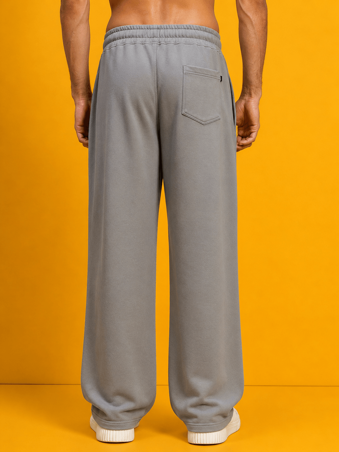 Back view of DRAPE TAILORED FIT JOGGERS GREY on a model, showcasing comfort and style against a bright yellow background.