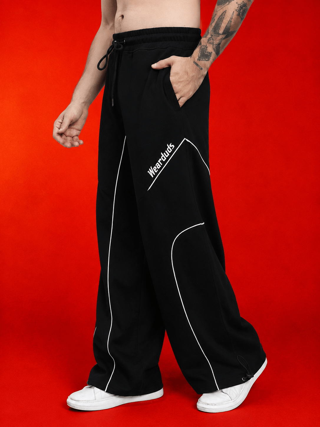 Model wearing SIGNATURE PIPING JOGGERS BLACK with contrast piping and relaxed fit against a vibrant red background.