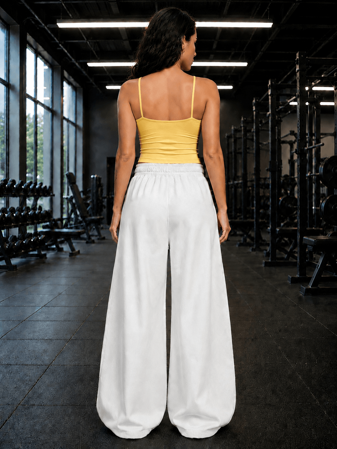 Back view of a woman wearing WOMEN SEAMLESS COTTON CROP-TOP YELLOW with loose white pants in a gym setting.