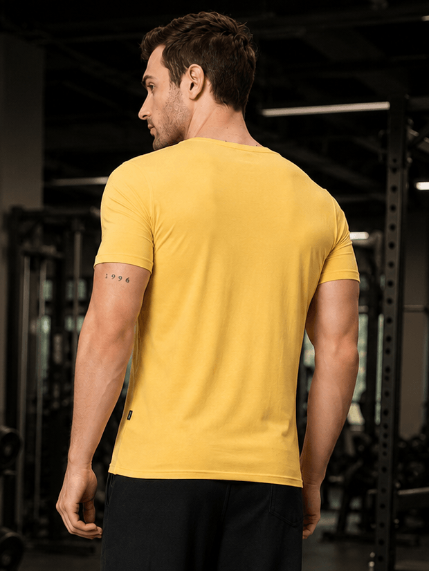 Back view of a man wearing RICKY REGULAR FIT T-SHIRT YELLOW in a gym setting, showcasing its vibrant color and fit.