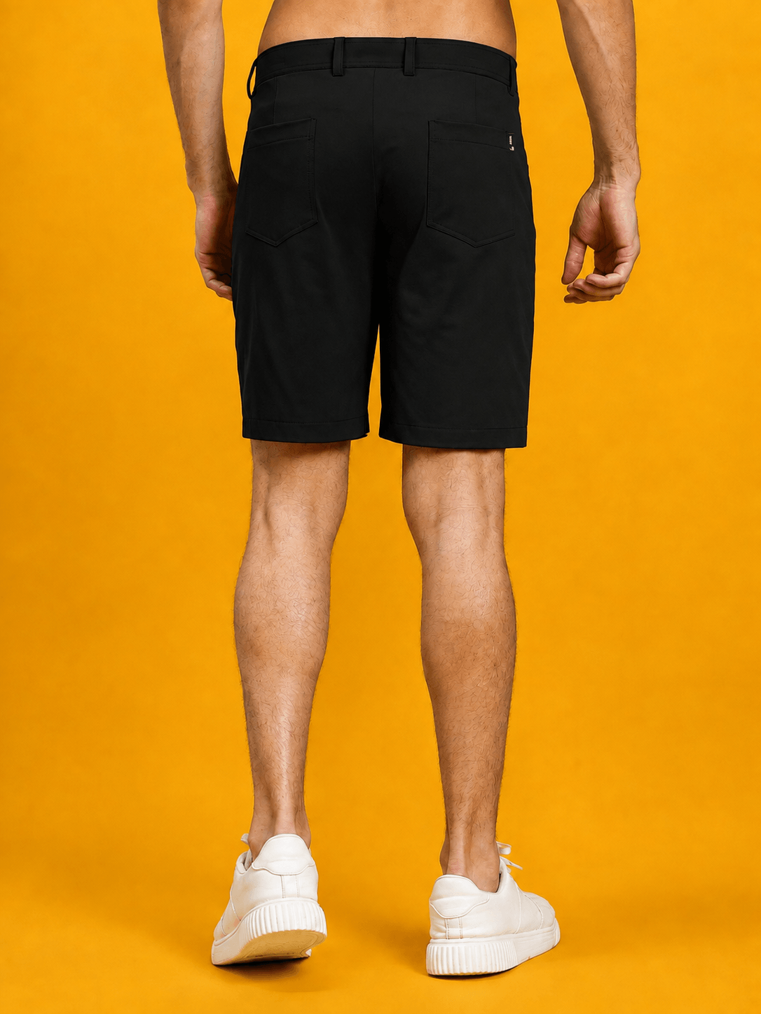 Back view of male model wearing PRIME FIT PERFORMANCE REGULAR SHORTS BLACK against a bright yellow background.