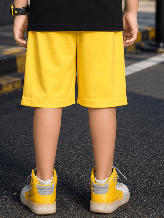 A child wearing MIDNIGHT BAT SHORTS FOR BOYS GIRLS YELLOW, showcasing the vibrant yellow fabric from a rear view.