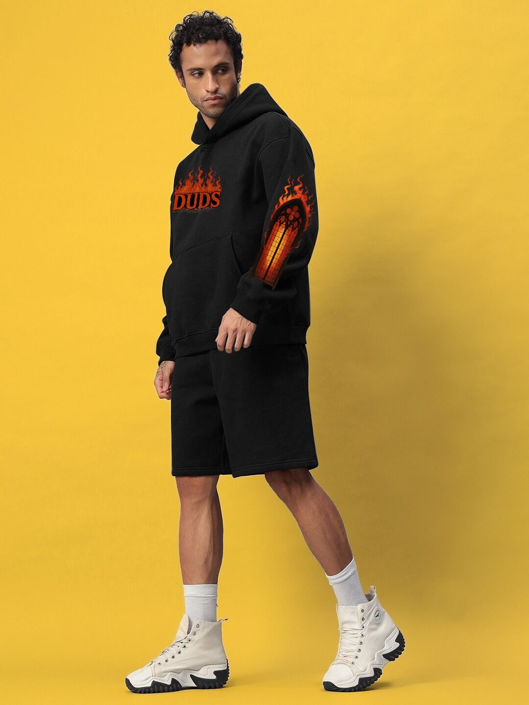 Model wearing FIRE NEVER KILLS THE LIGHT FLEECE CO-ORD BLACK with bold design on a yellow background, showcasing street-luxe style.