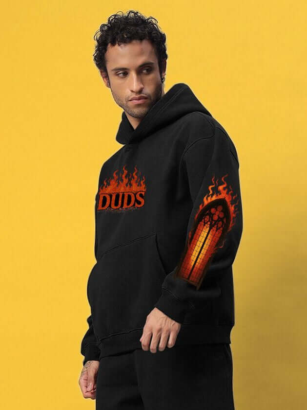 Man wearing FIRE NEVER KILLS THE LIGHT PRINTED FLEECE HOODIE BLACK, featuring bold graphic and sleek design for street-style fashion.