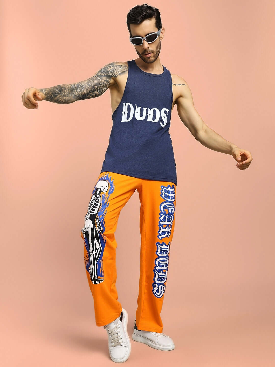 Person wearing FLAMING SKELETON PRINTED RELAXED FIT JOGGER ORANGE by DUDS with sunglasses and tank top.