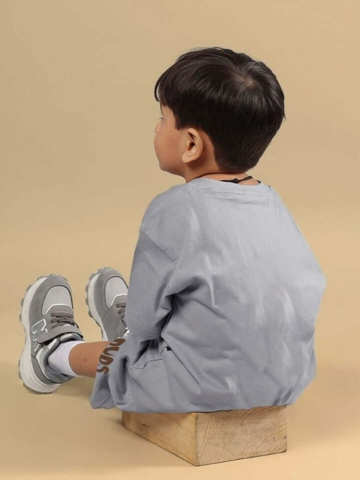 Boy wearing a grey FLINT BUNNY T-SHIRT FOR BOYS AND GIRLS, seated on a wooden block, showcasing casual comfort and style.