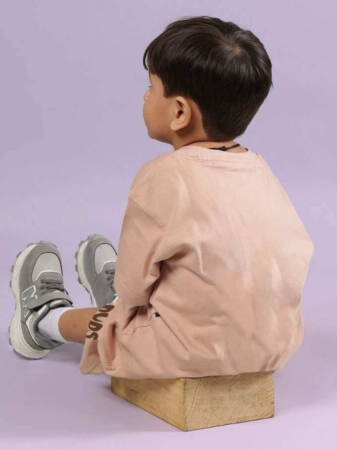 Child wearing FLINT BUNNY T-SHIRT FOR BOYS AND GIRLS BEIGE sitting on a wooden block against a purple background