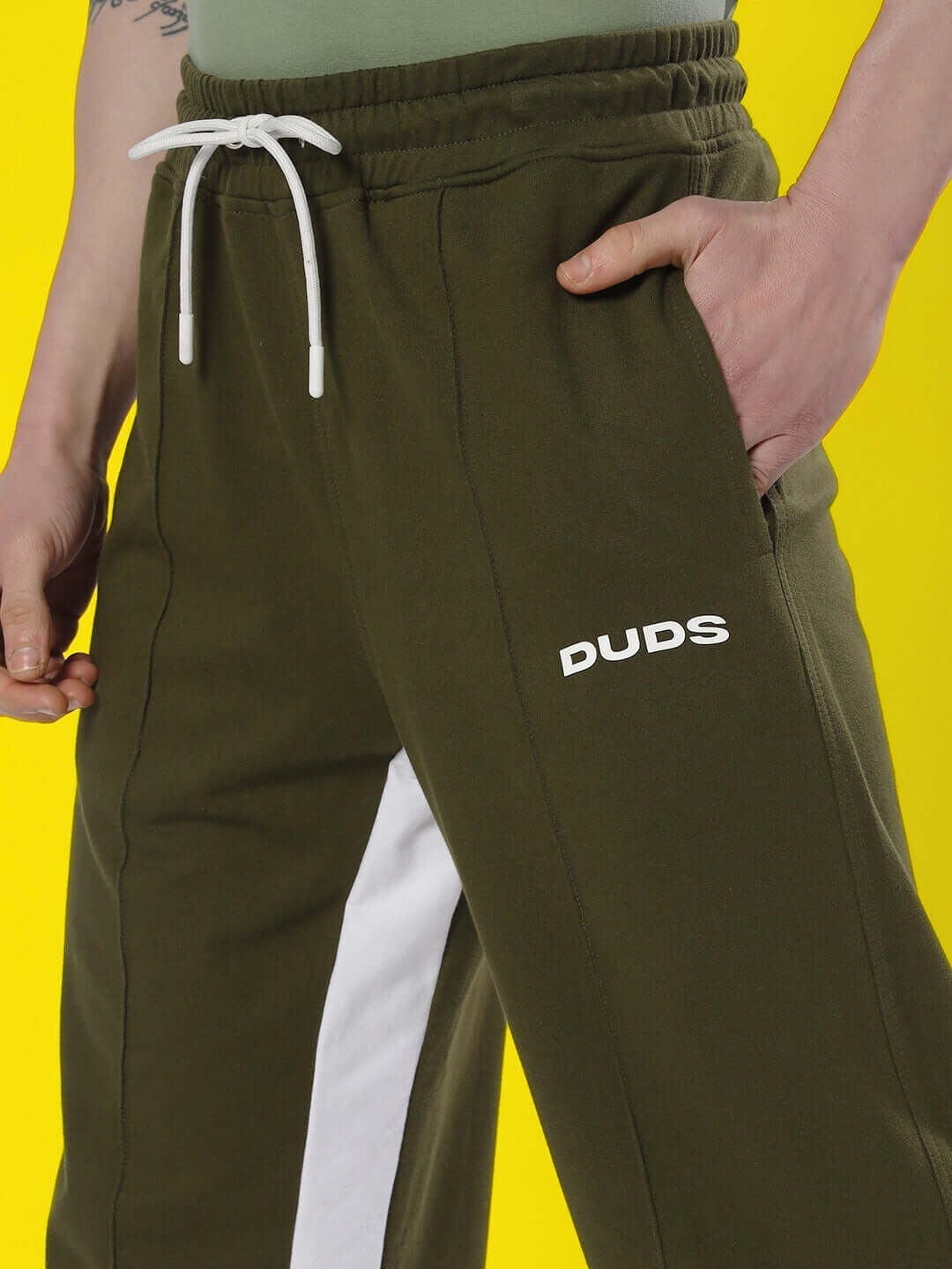 Person wearing olive green floppy flared contrast joggers with white stripe detail from DUDS, featuring an adjustable drawstring waistband.