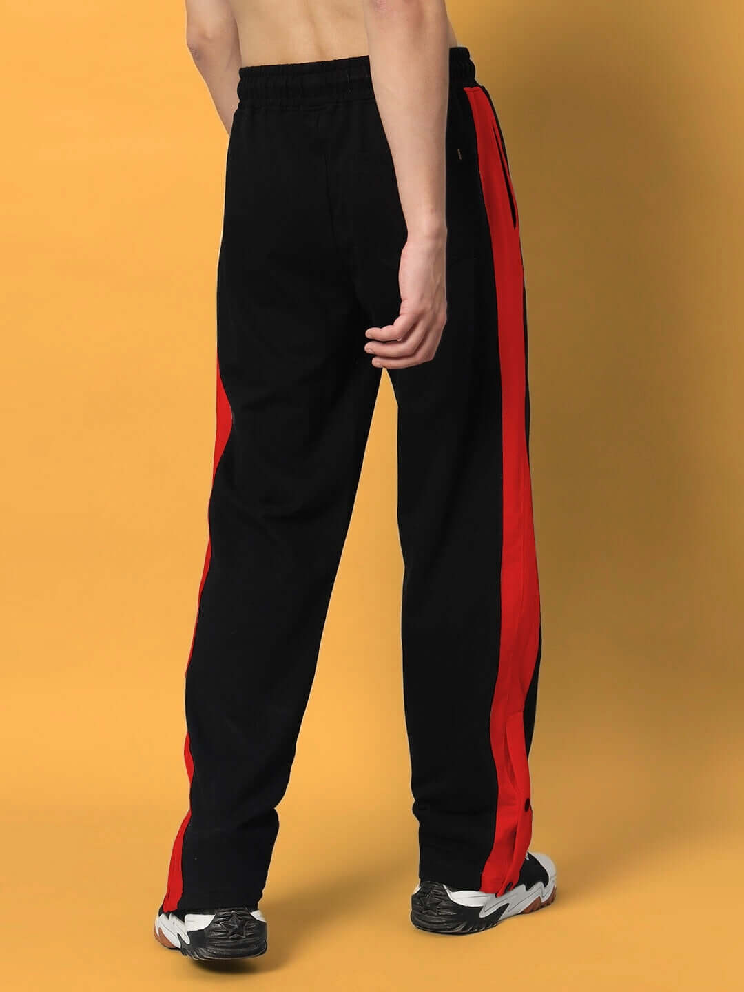 Back view of a person wearing FLURRY CONTRAST JOGGERS in black and red, highlighting the side stripe detail on a warm background.