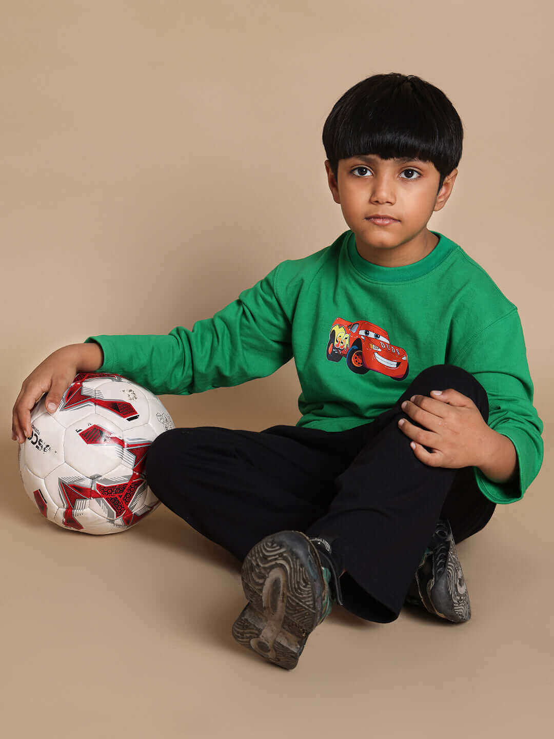 Child wearing a green-black Formula 1 co-ord set sitting with a soccer ball.