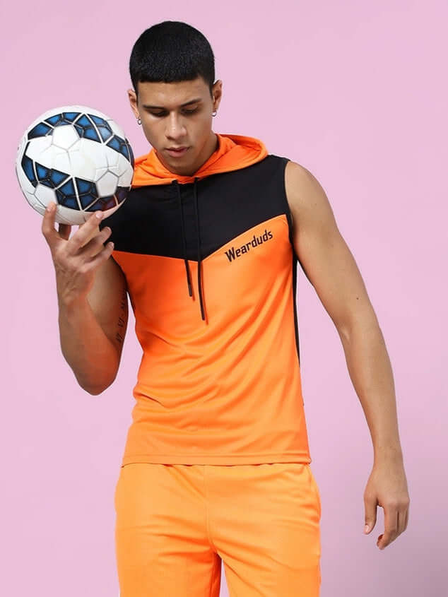 Man wearing FRANKY GYM T-SHIRT ORANGE BLACK with a soccer ball on pink background.