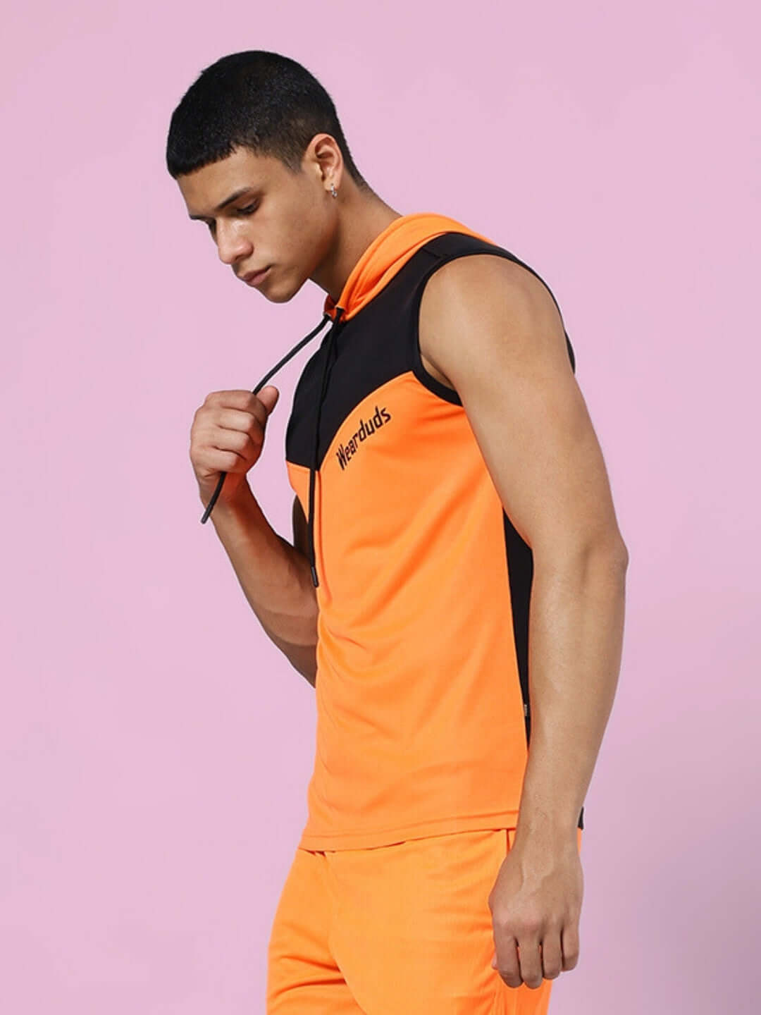 Man wearing FRANKY GYM T-SHIRT ORANGE BLACK, side view with pink background.