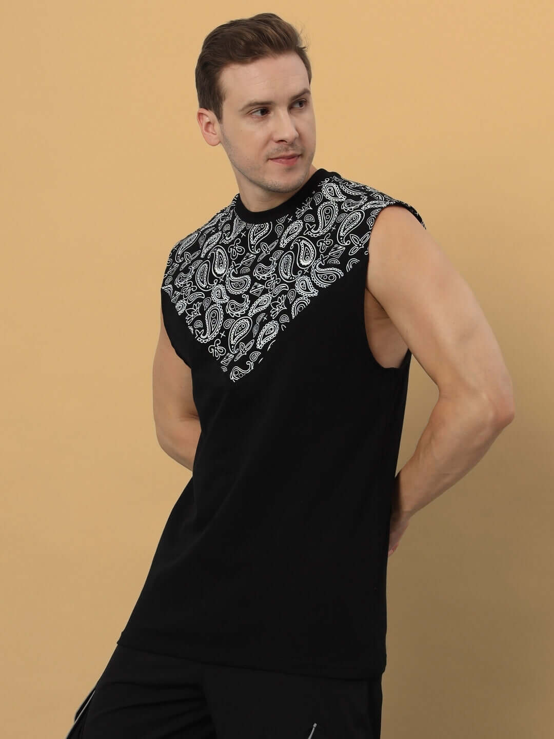 Man wearing a black oversized sleeveless T-shirt with paisley design, made of 97% cotton and 3% elastane. Fashionable and comfortable summer wear.