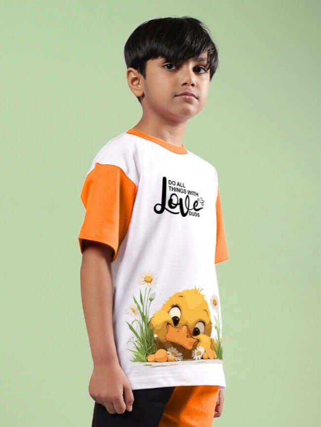 Boy wearing FRIENDSHIP BUCKET T-SHIRT FOR BOYS & GIRLS WHITE-ORANGE with cartoon design, against green background.