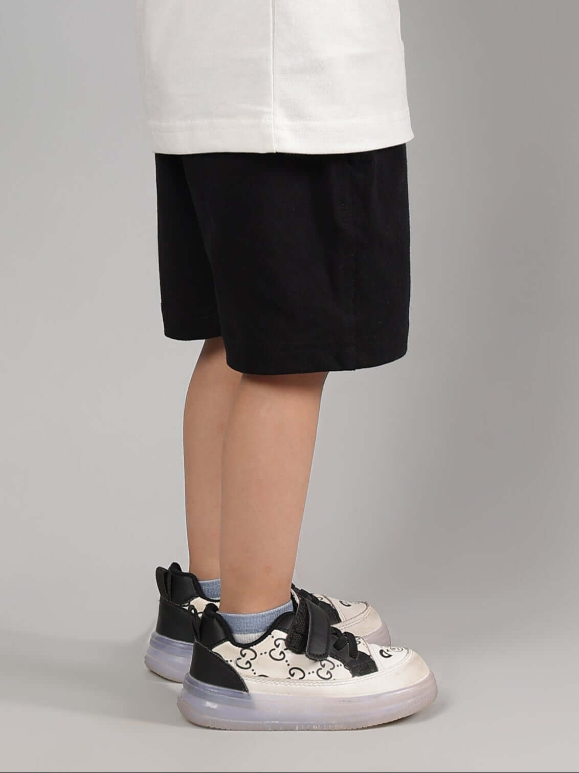 Child wearing black printed summer shorts with sneakers, side view.