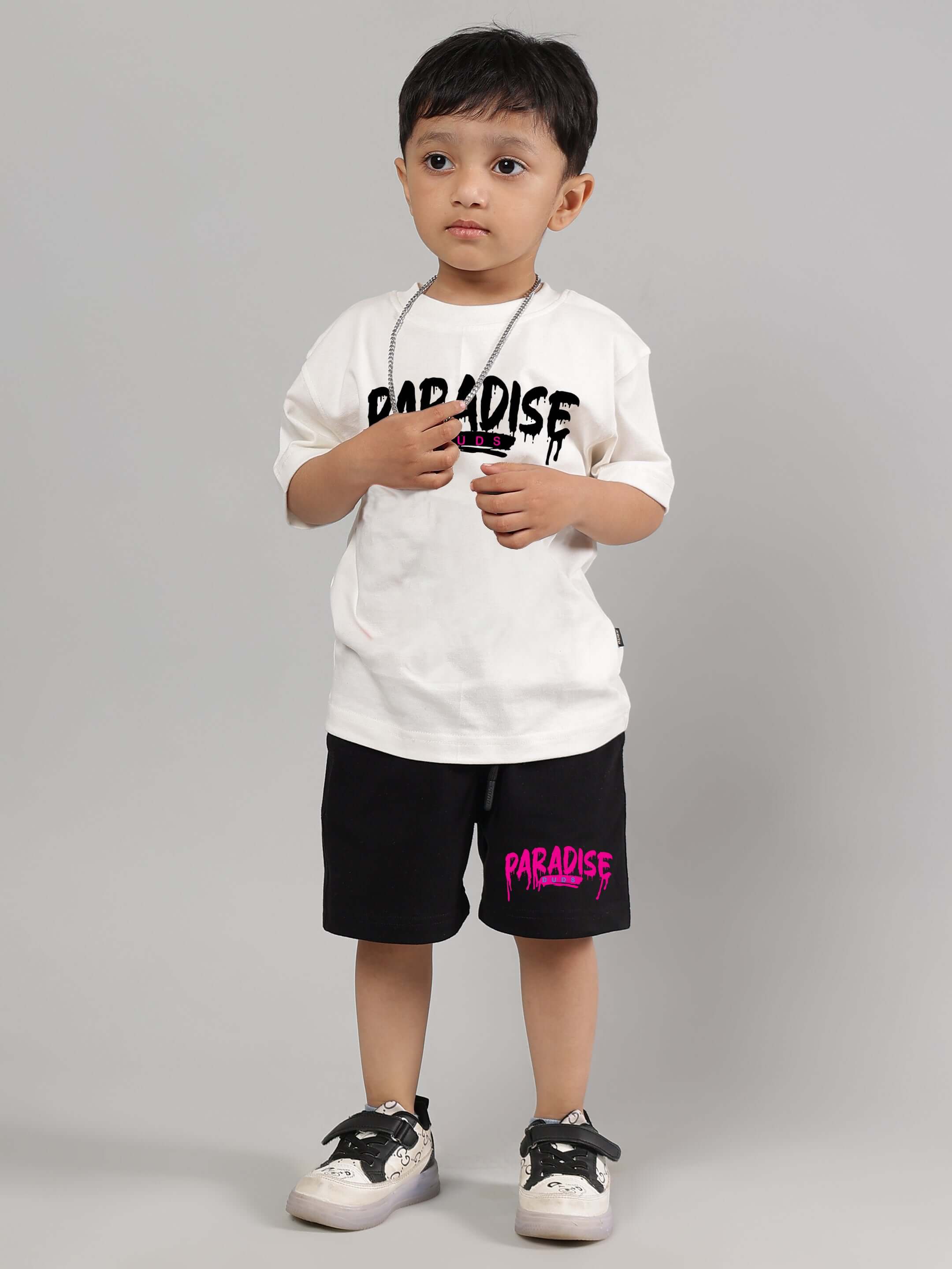 Young child wearing an off-white Fulness Paradise t-shirt and black shorts, showcasing casual style for boys and girls, standing against a gray background.