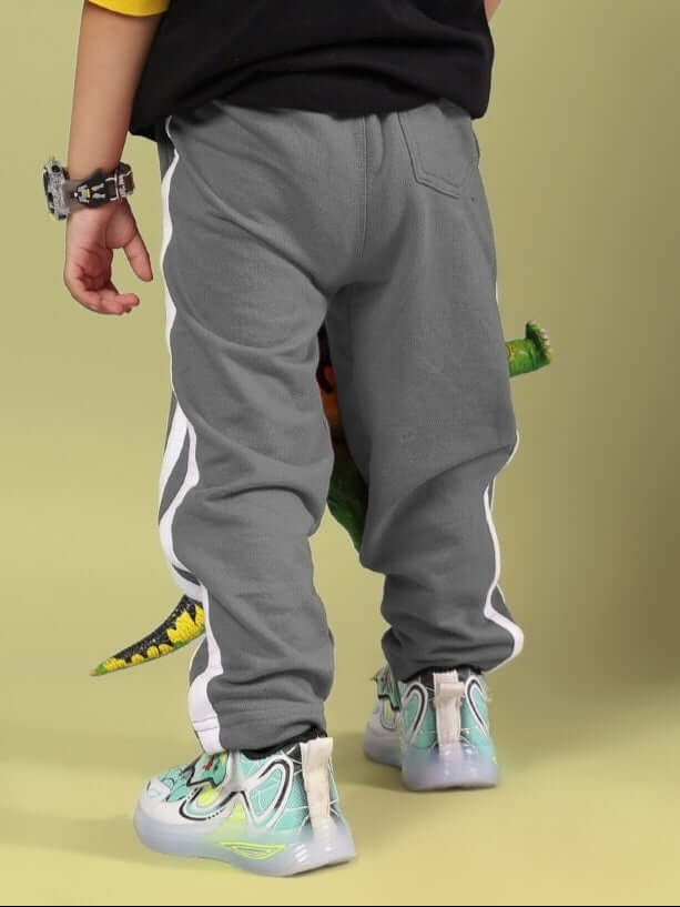 Child wearing grey FUTURE ICON joggers with dinosaur tail on a yellow background, showcasing playful design for kids.