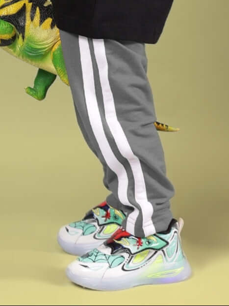 Grey Future Icon Jogger for Boys & Girls with white stripes, paired with colorful sneakers, shown in playful setting.