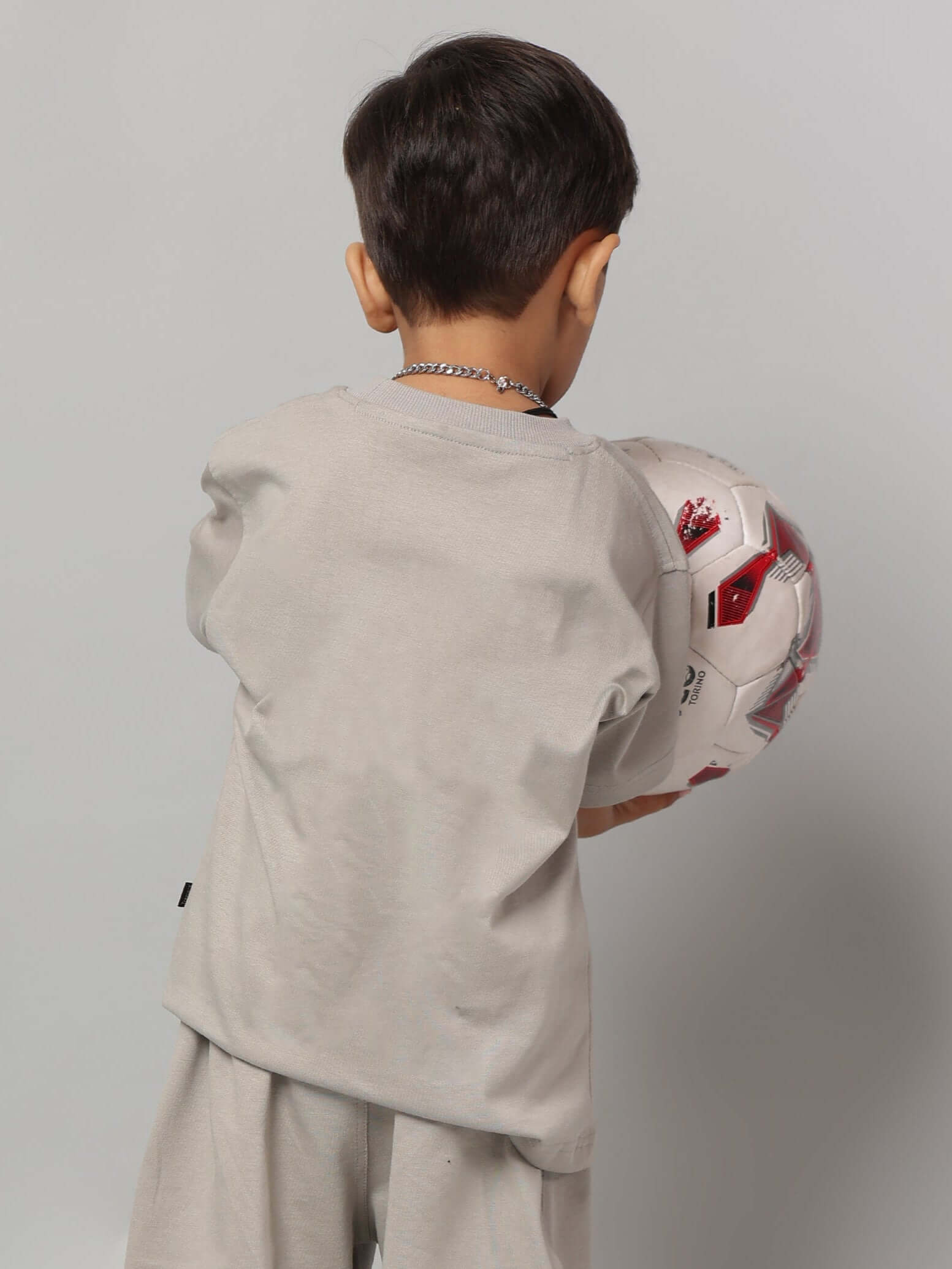 Child wearing grey futuristic t-shirt holding a soccer ball, showcasing modern, tech-inspired kids’ fashion for boys and girls.