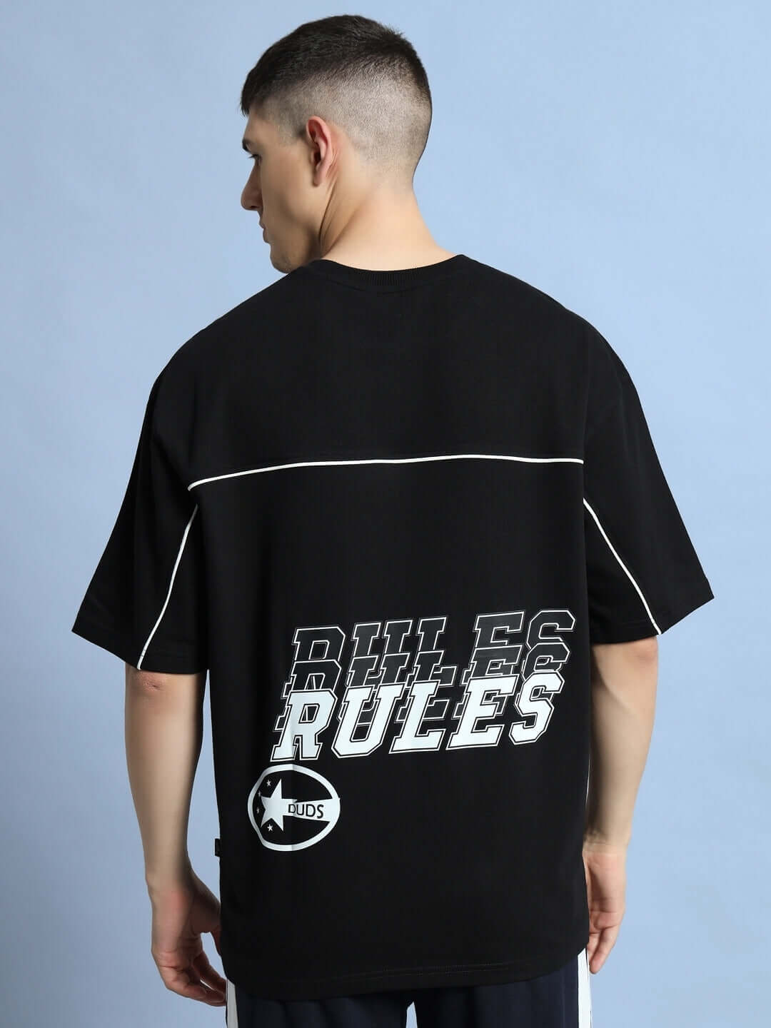 Model wearing black oversized t-shirt with 'RULES' graphic on back, offered by DUDS, available in custom fit for prepaid orders.