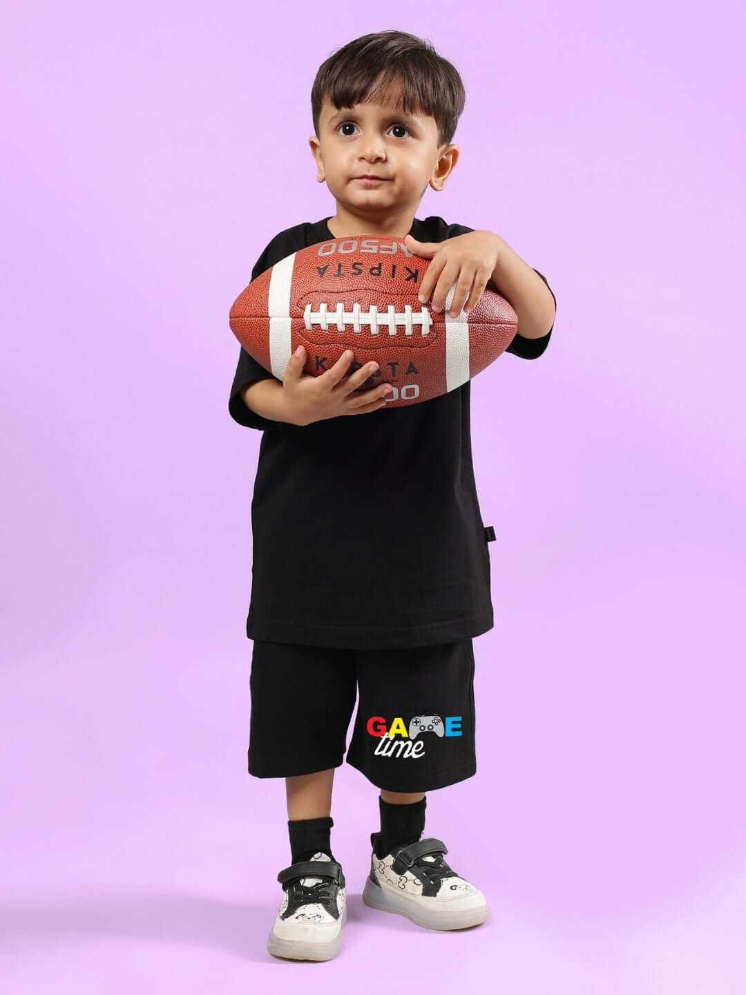 Young child wearing GAME FINISHER CO-ORD FOR BOYS & GIRLS BLACK holding a football on a purple background.