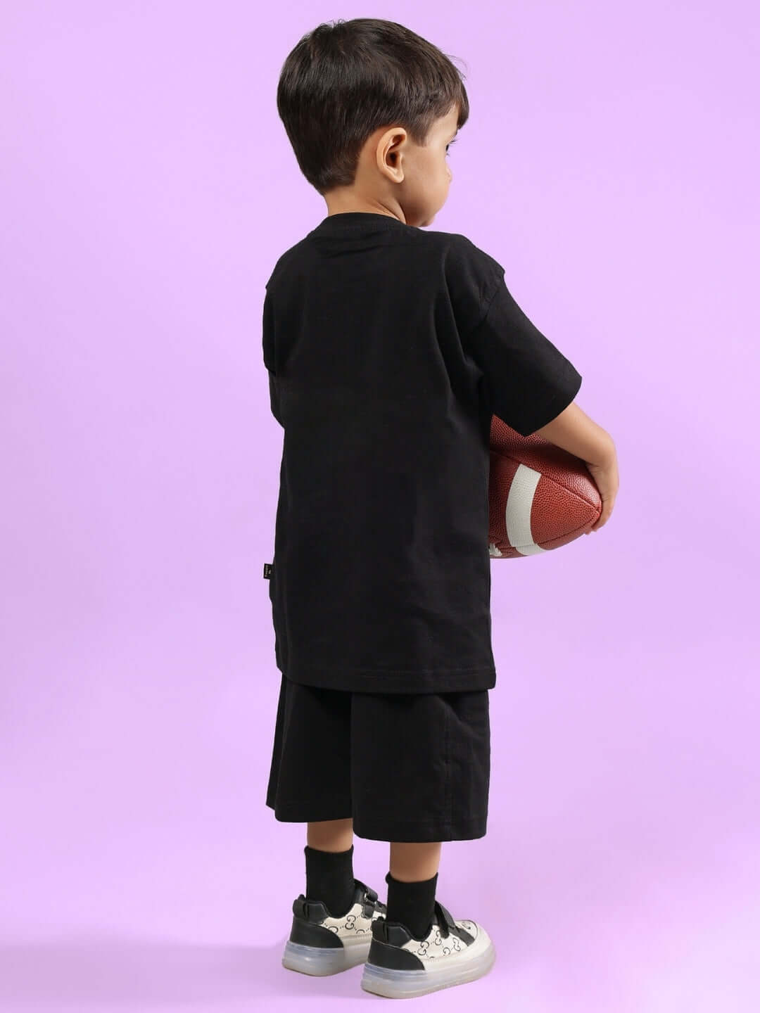 Child wearing GAME FINISHER CO-ORD FOR BOYS & GIRLS BLACK holding a football on a purple background