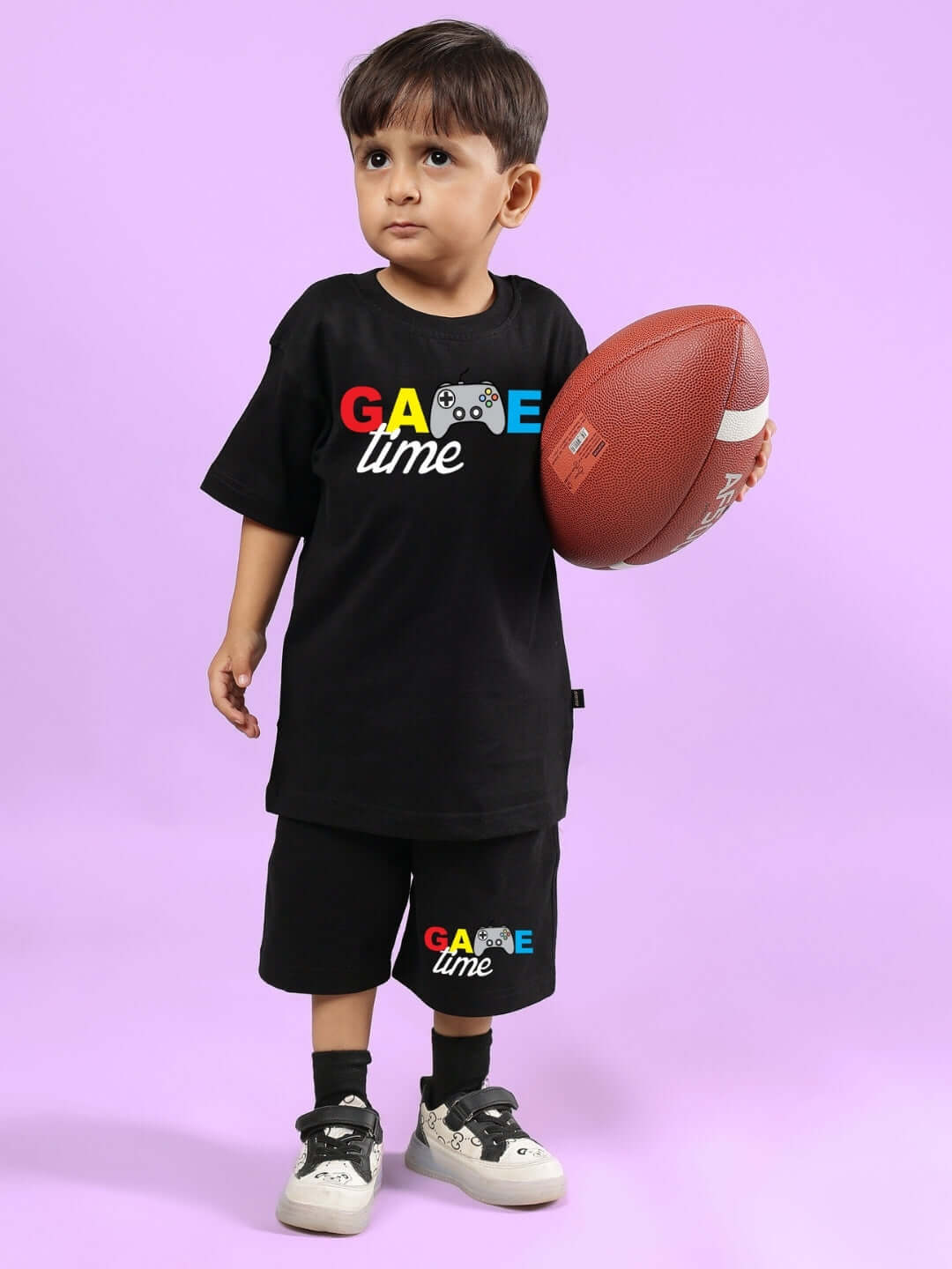 Child wearing GAME FINISHER SHORTS FOR BOYS & GIRLS BLACK, holding a football.