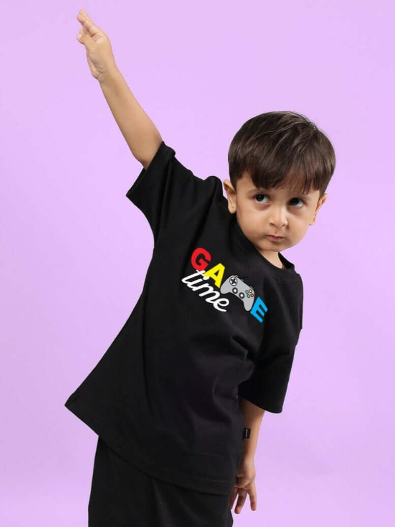 Young boy wearing GAME FINISHER T-SHIRT FOR BOYS & GIRLS BLACK raising his arm playfully against a purple background.