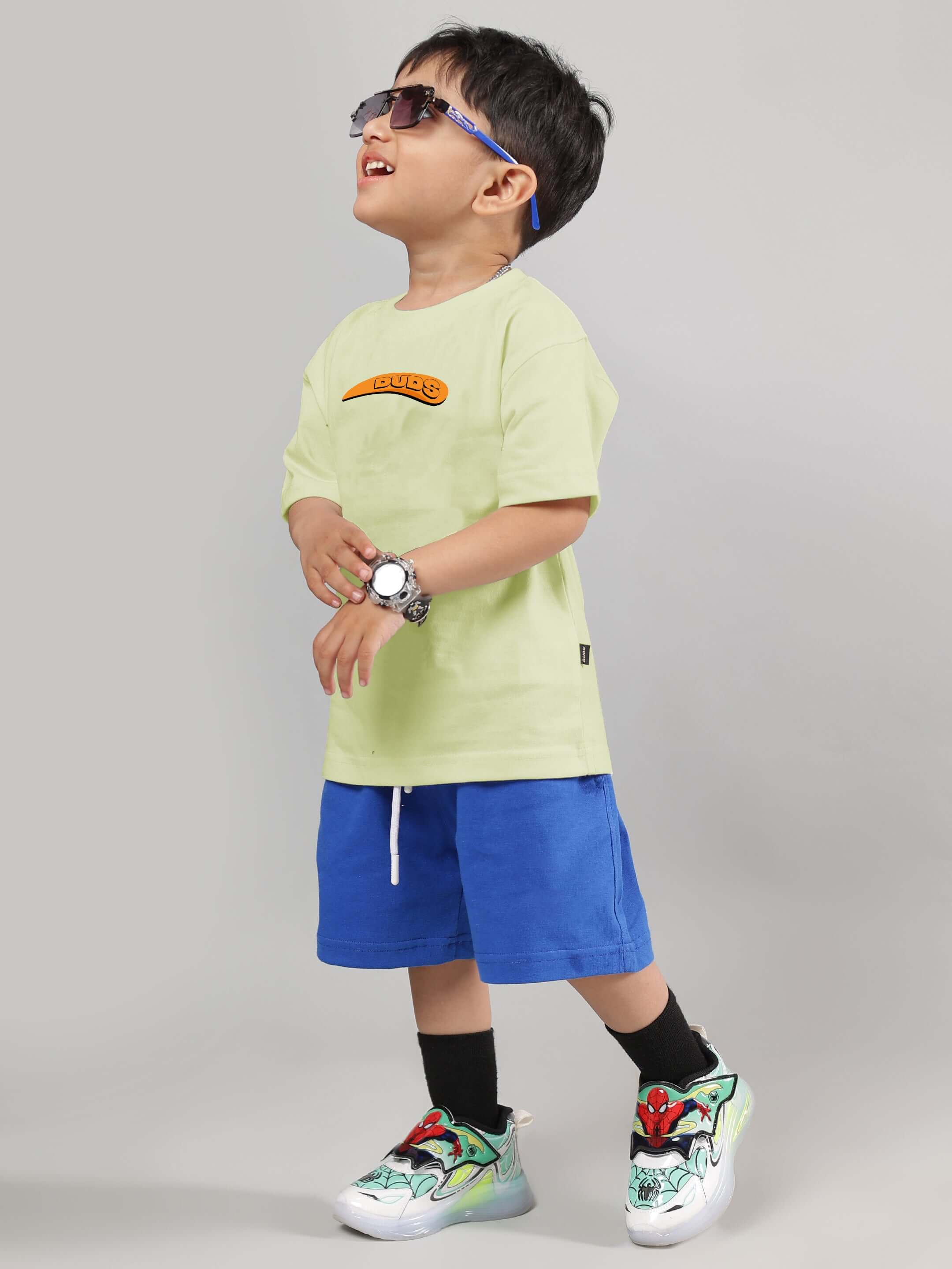 Child wearing Garfield co-ord in celery and ice blue, featuring a graphic design with sneakers, sunglasses and a matching watch.