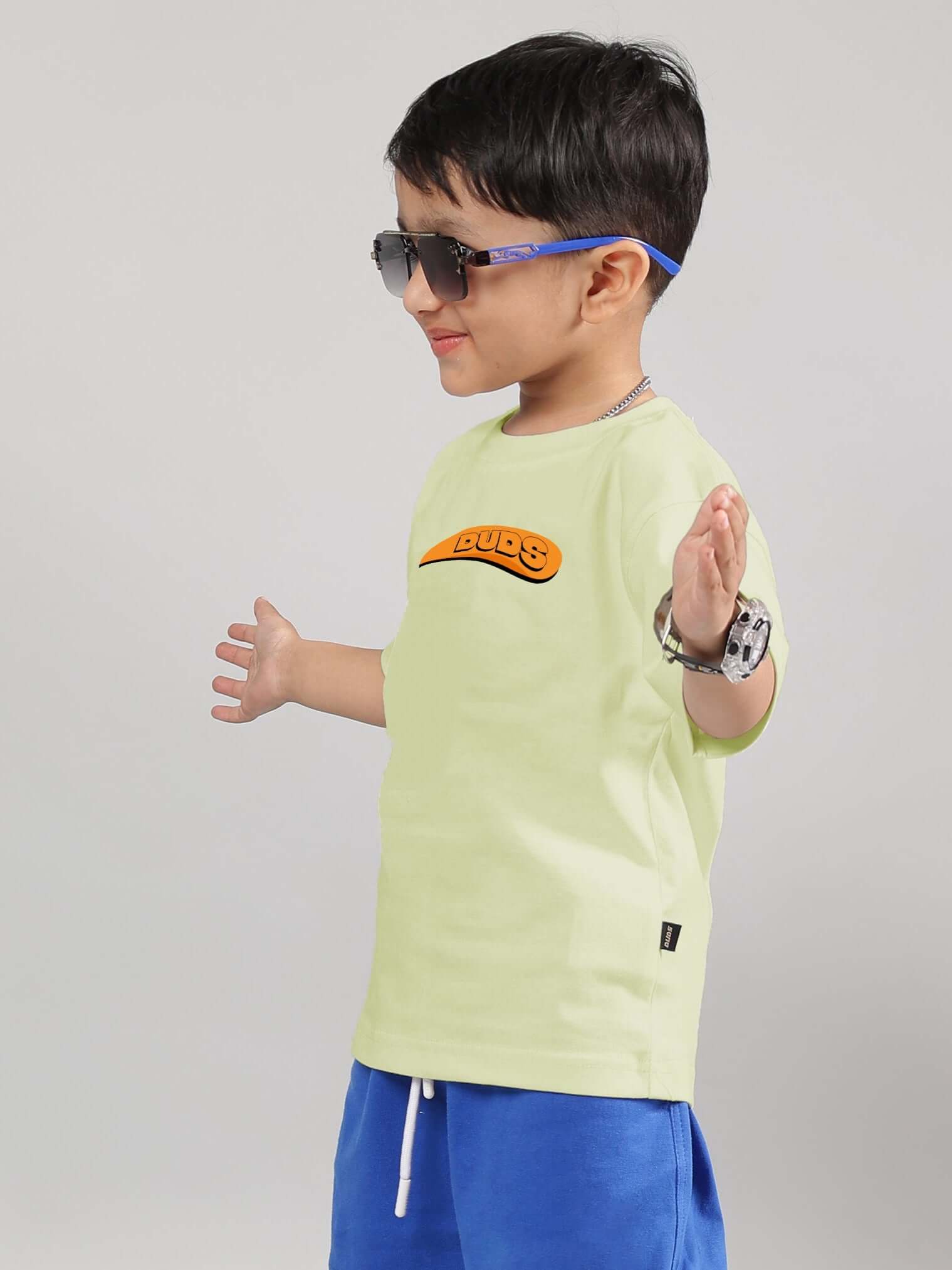Boy wearing GARFIELD T-SHIRT FOR BOYS GIRLS CELERY-ICE in celery shade with graphic, sunglasses, and blue shorts.