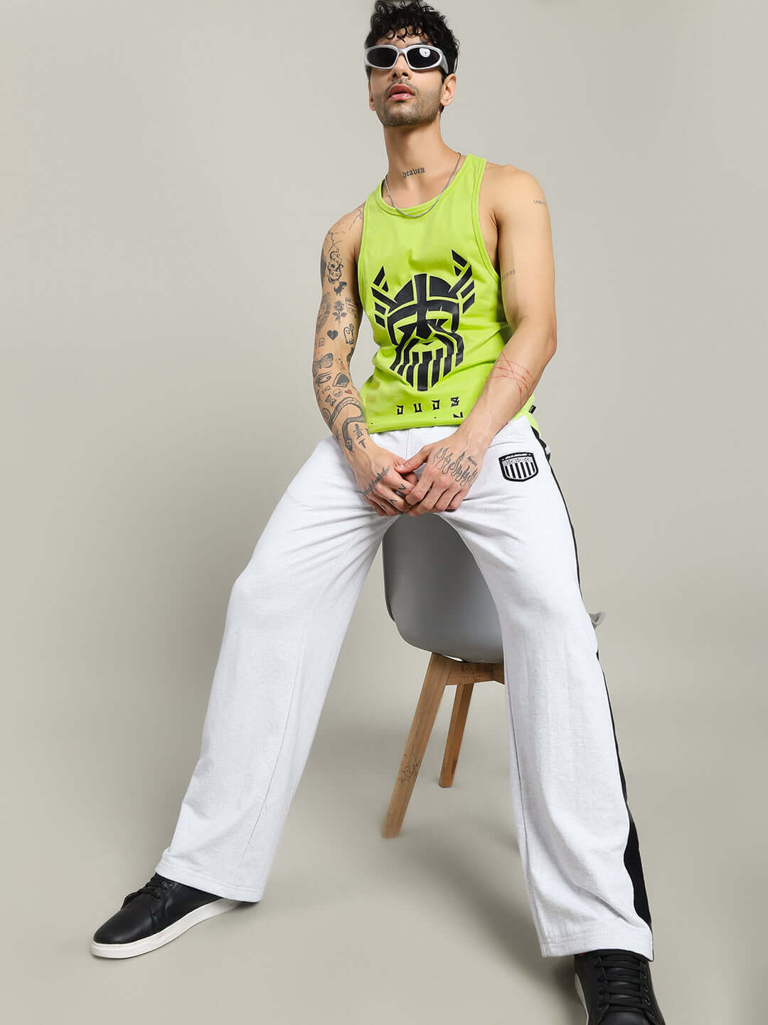Man wearing neon green Gladiator gym t-shirt with tribal design, paired with white pants and black sneakers, sitting on a chair.