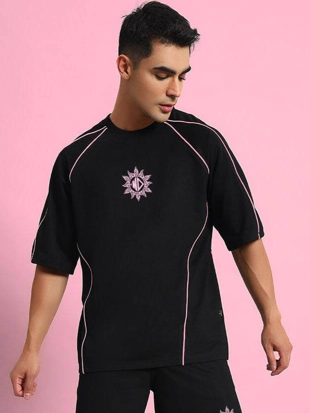 Man wearing GLARE black co-ord set, featuring premium cotton French terry fabric with pink accents in a stylish pose against a pink background.