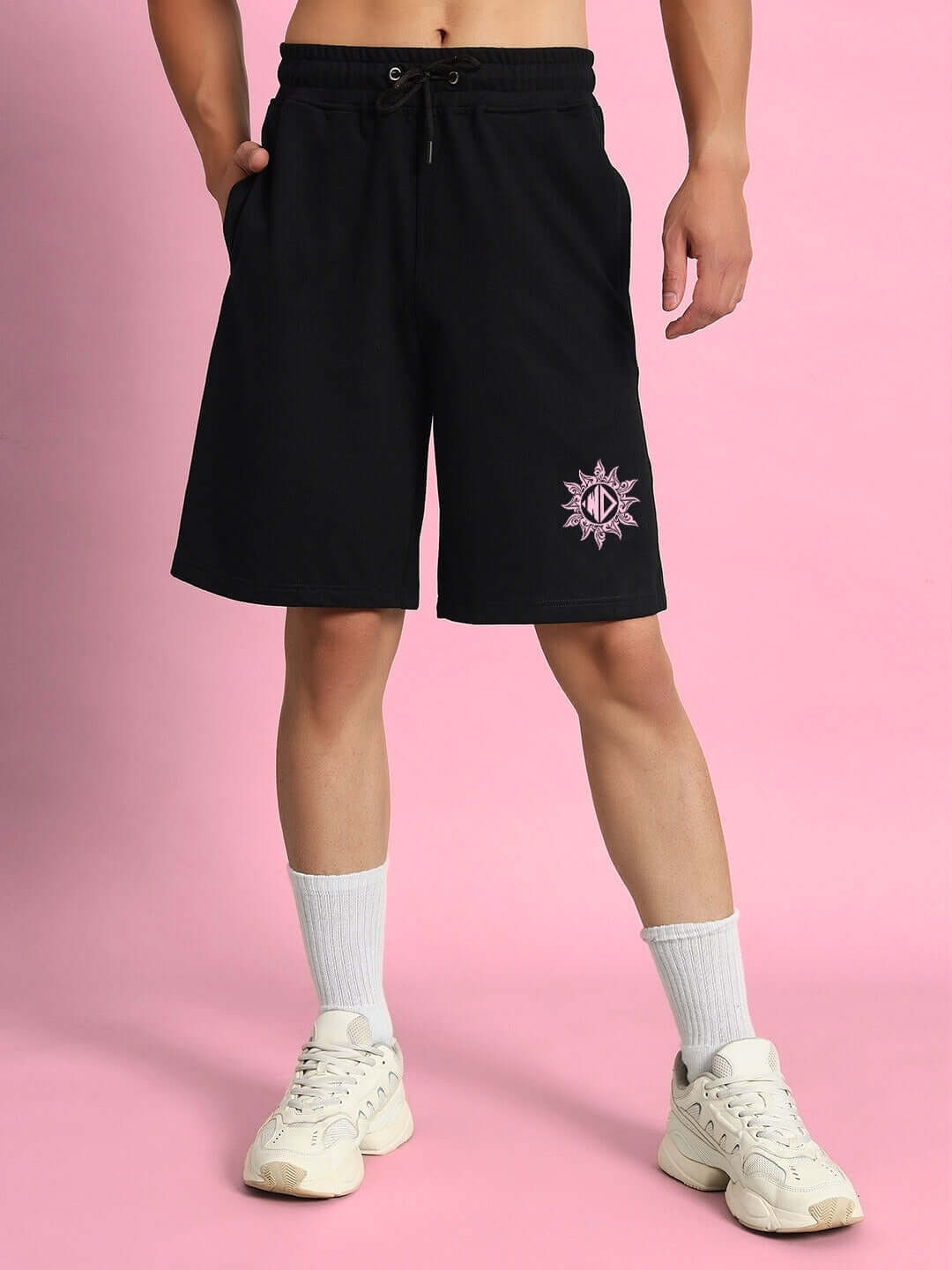 Model wearing GLARE COTTON TERRY CO-ORD SET BLACK shorts, sporty and stylish design, against a pink background.