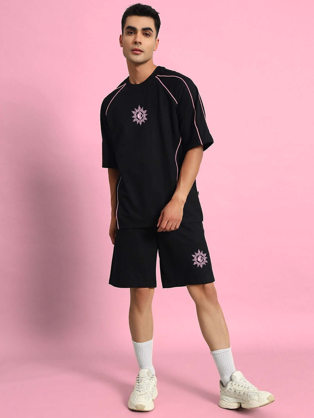 Model wearing GLARE REGULAR FIT SHORTS BLACK with matching black top on pink background.
